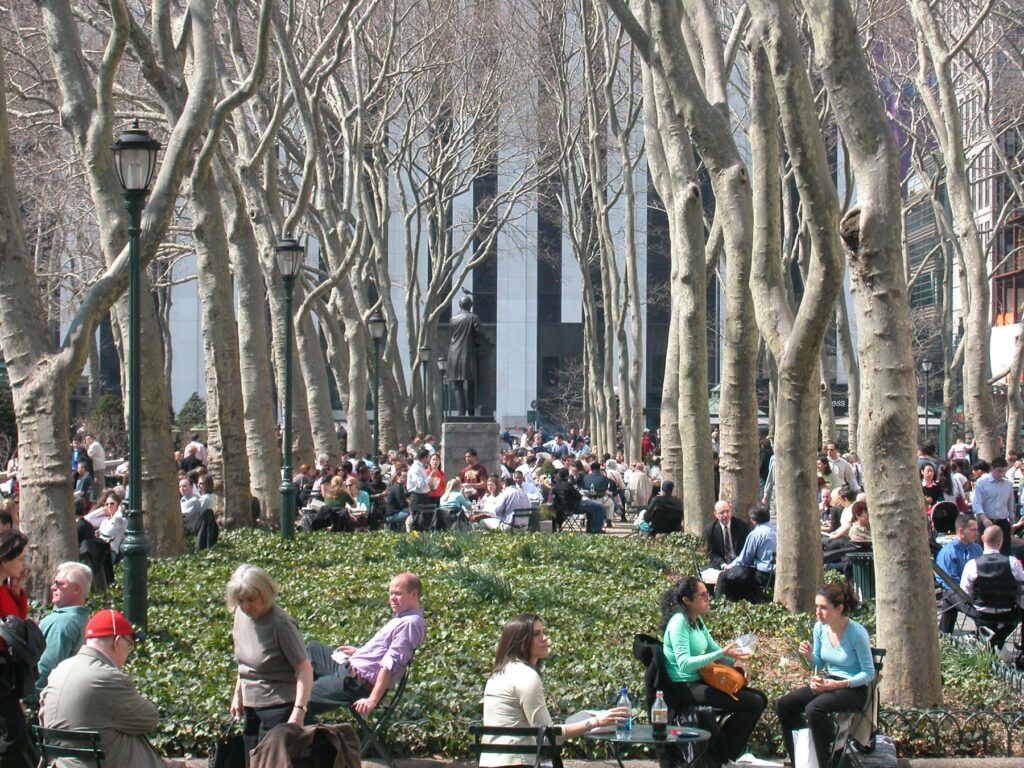Multiple people relaxing in a park with barren trees in New York City.