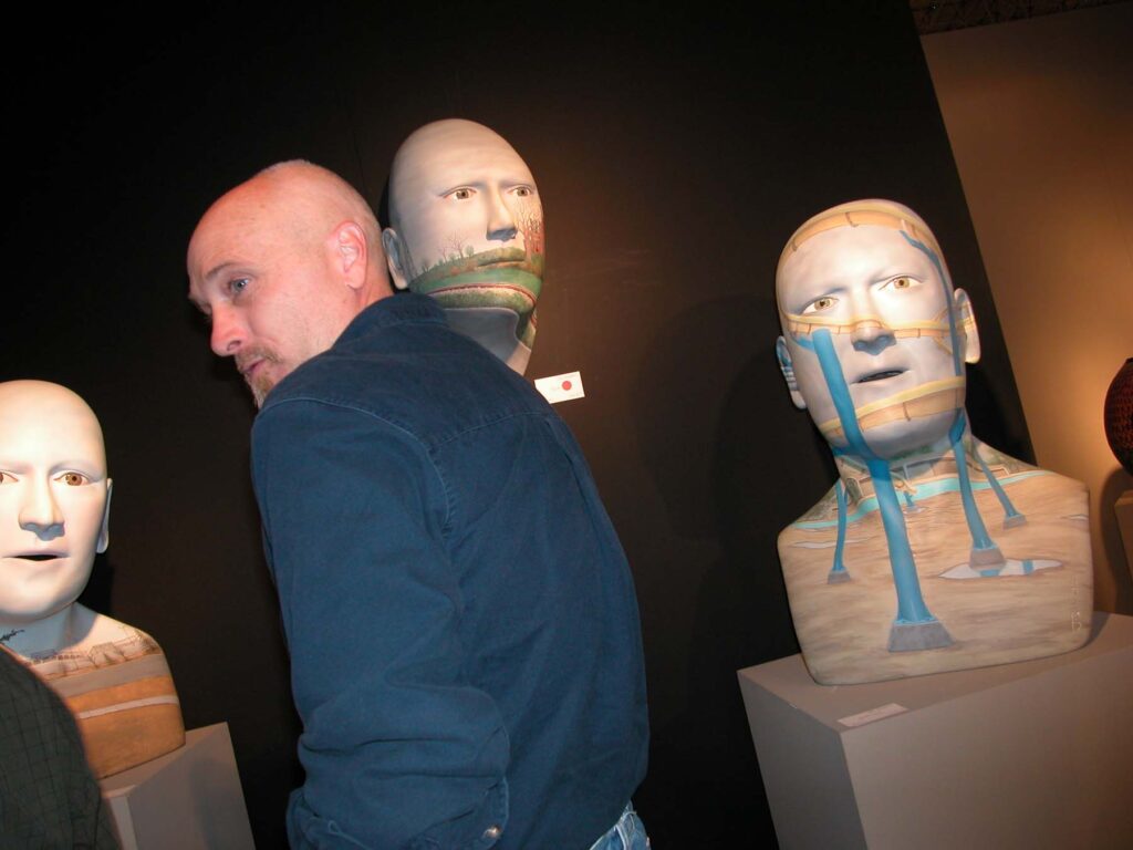 Bald man amidst grouping of bald sculptures in Chicago Art Expo.