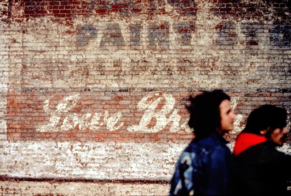 Two motorcycle riders in front of an old brick storefront with words Lowe Brothers, photographed in Davenport, Iowa, 1977.
