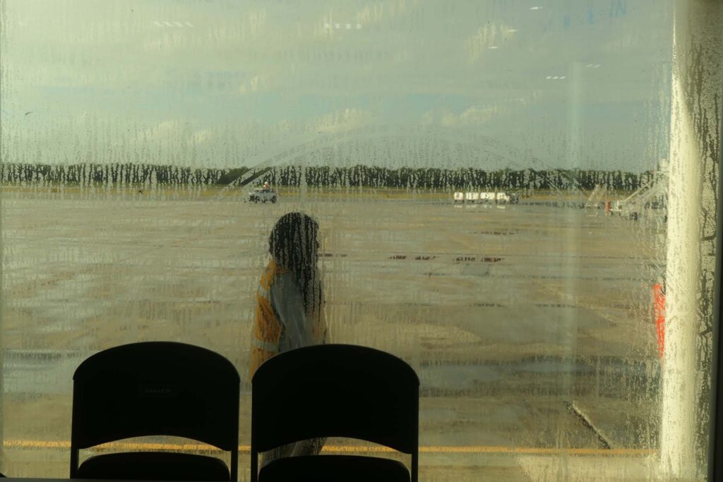 Figure in front of two chairs through window looking at airport runway