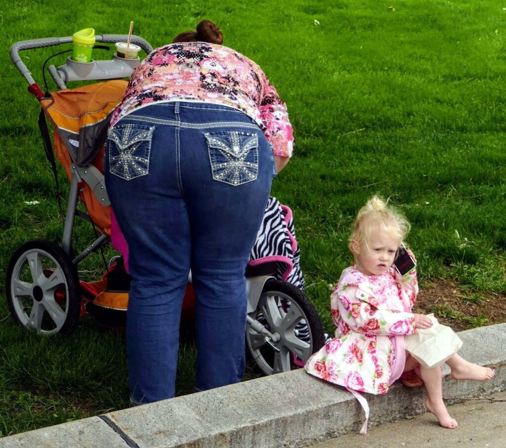 Little girl playing with mother's phone while mother is attending to another child.